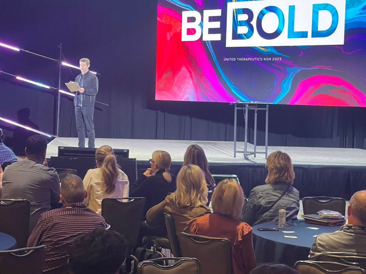 Joe Cummings on stage at a national sales meeting with the audience seated at round tables