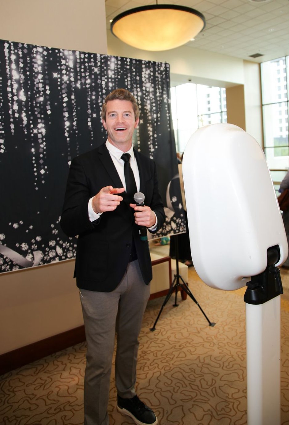 Joe Cummings in a suit with a microphone engaging guests at a formal corporate brand event